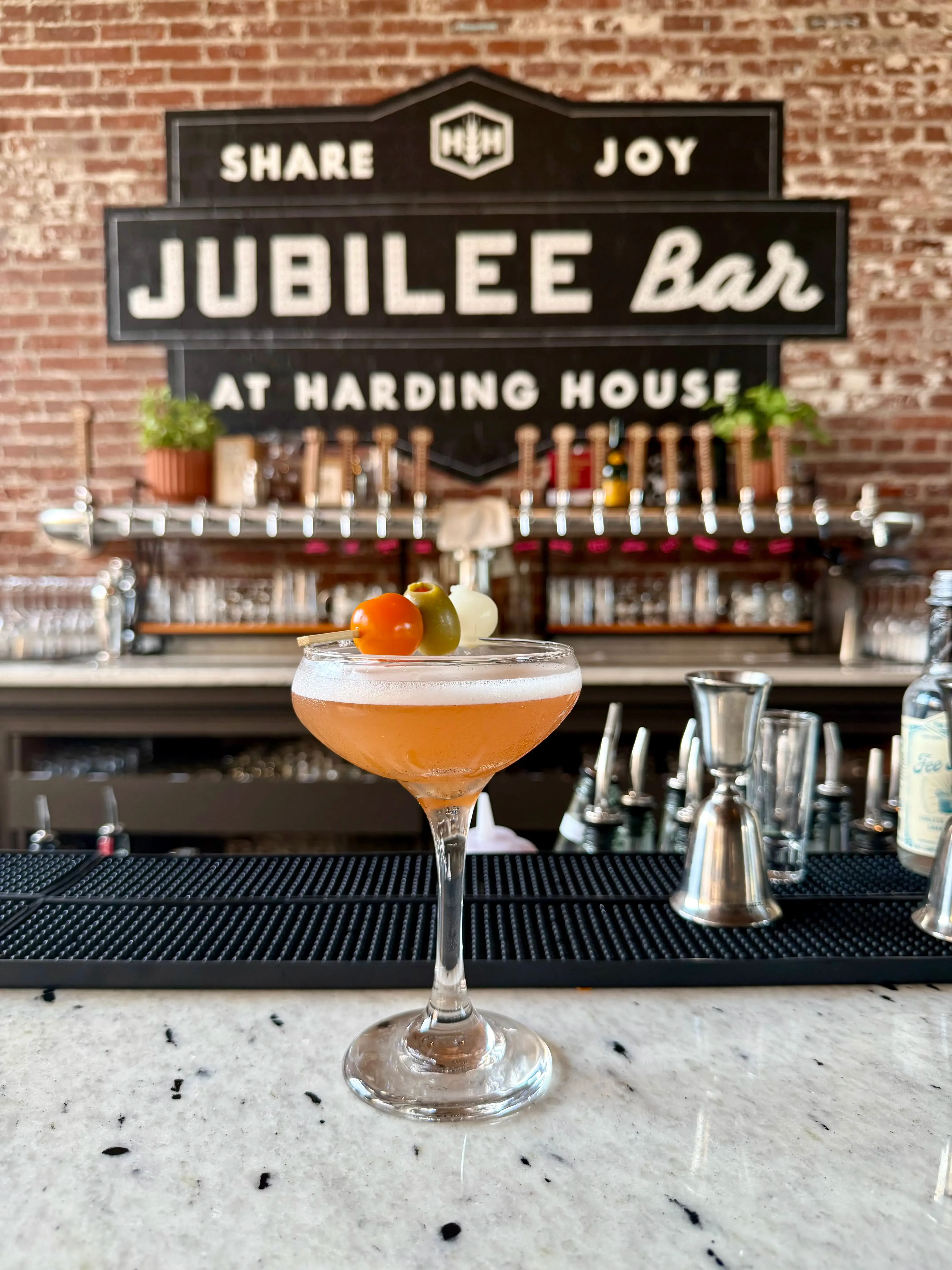 A coupe cocktail on the bar in front of The Jubilee Bar at Harding House sign.